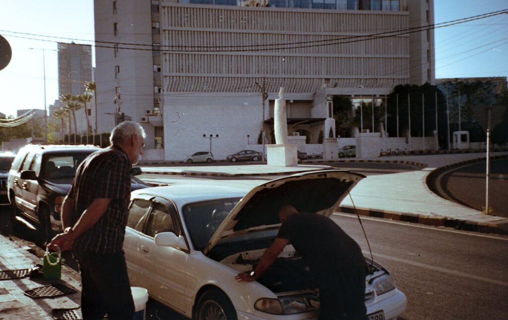 Two men are working on a car in the street